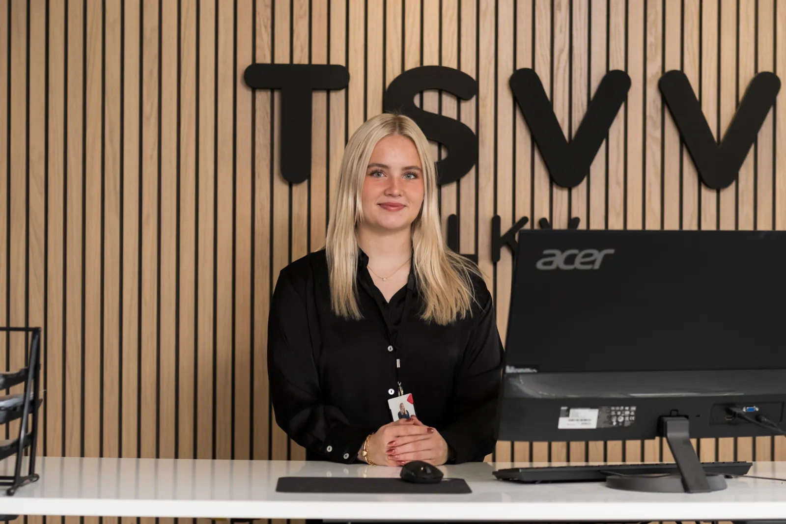 TSVV:n välittäjä toimiston vastaanottotiskillä TSVV-logoseinän edessä